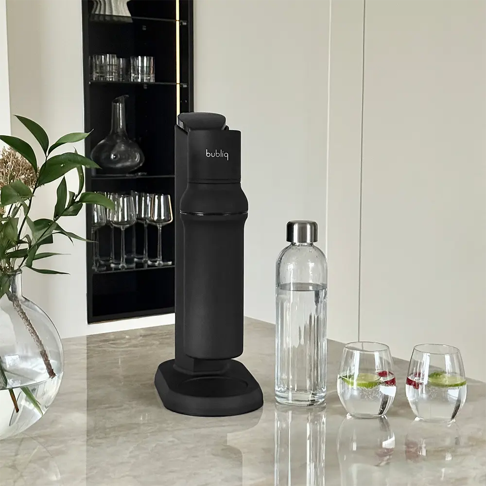 Sodavandsmaskine med glasflaske på marmorbord med 2 glas danskvand