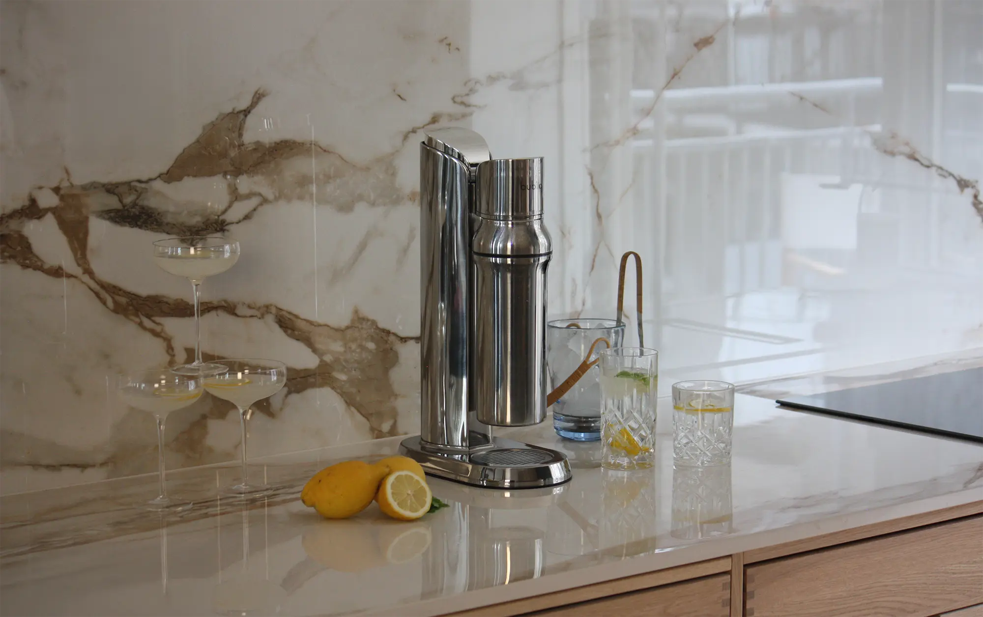 Wassersprudler mit Glasflasche mit zwei Gläsern Sprudelwasser und Zitronen auf dem Tisch